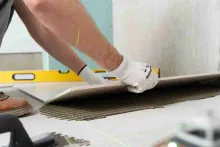 Tiler applying floor tiles using German polymer-based tile adhesive for strong and durable bonding